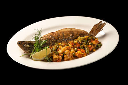 Baked fish with vegetables in a white plateの写真素材