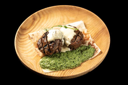 Meat medallions on a wooden plate with spinachの写真素材