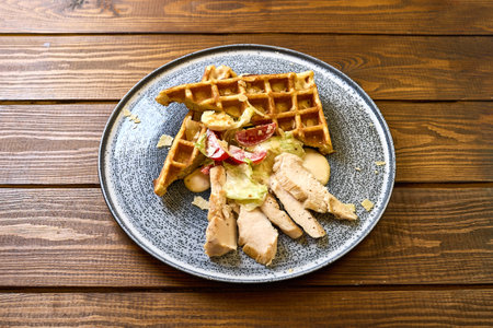 A savory dish featuring a crispy waffle topped with grilled chicken, a creamy salad, and parmesan cheese shavingsの写真素材