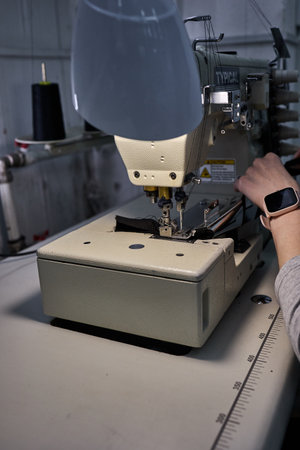 A worker's hands guide fabric through an industrial sewing machine in a textile factory.