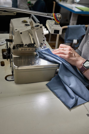 A close-up view of an industrial overlock machine stitching the edge of blue fabric