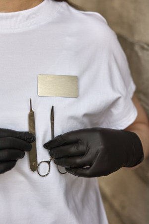 A professional wearing black gloves holds surgical instruments in front of a white uniform with a...