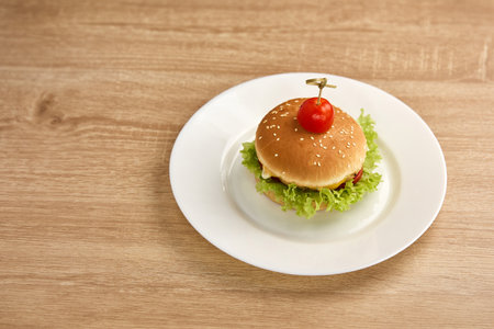 A delicious cheeseburger with lettuce, tomato, and cheese, served on a white plate.の写真素材