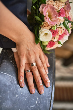 Hands of a couple elegantly adorned with wedding rings, gently holding a bouquet of flowers, symbolizing unity and love, commitment conceptの写真素材