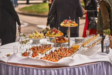 Banquet table outdoors featuring an assortment of appetizers, fruits, and drinks, prepared for a celebration event, festive atmosphere, catering joy conceptの写真素材