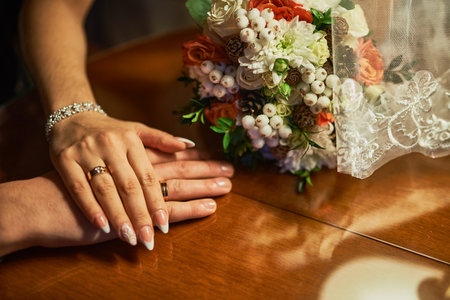 Wedding moment with couple's romantic hands, bouquet on wooden table, elegant rings, love, marriage, unity, celebration, intimate, wedding conceptの写真素材