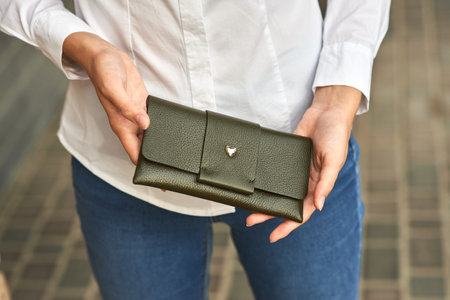Elegant green leather wallet held by woman in white shirt and blue jeans, outdoor street scene conceptの写真素材