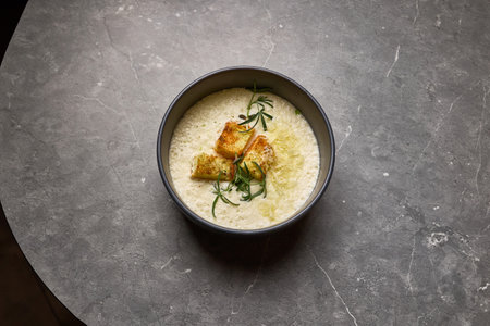 Tasty creamy soup topped with crispy croutons and rosemary, presented in a bowl on gray stone, birdâs eye view, gourmet meal conceptの写真素材