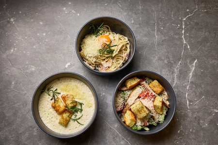Elegant dining dishes featuring gourmet pasta, salad, and creamy soup served in bowls on marble...