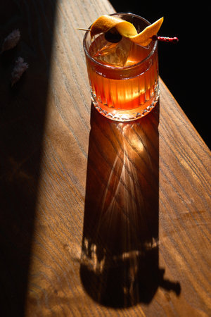 A rich amber cocktail served in a textured glass. The drink is garnished with a twist of citrus peel...