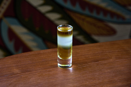A beautifully layered cocktail in a shot glass, elegantly placed on a rustic wooden table, perfect for bar settings and drink enthusiasts.の写真素材
