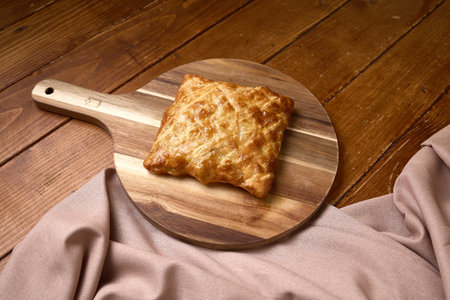Crispy and flaky square puff pastry with a golden-brown crust, served on a rustic wooden paddle over...