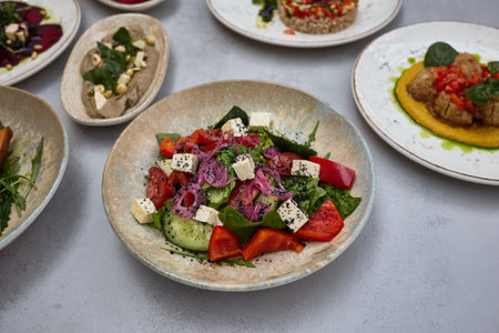A vibrant Greek salad with feta cheese, cherry tomatoes, cucumber, red onions, and fresh greens, garnished with black sesame seeds.の写真素材
