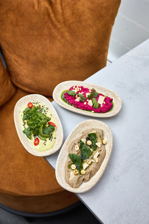 A beautifully plated trio of hummus varieties, including beetroot, avocado, and mushroom, garnished...