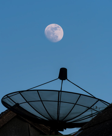 Near full moon in late evening with clear blue sky and sattellite dish.の写真素材