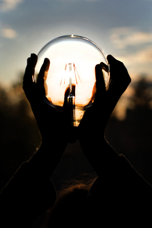 Energy light bulb from sunset on hand concept