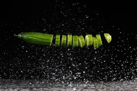 Sliced cucumber with splashing water or explosion flying in the air isolated on black background