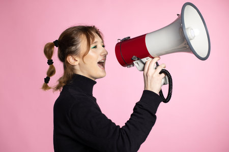 Funny young female shouting through megaphone. Young woman using loudspeaker on colored backgroundsの写真素材