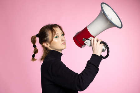 Funny young female shouting through megaphone. Young woman using loudspeaker on colored backgroundsの写真素材