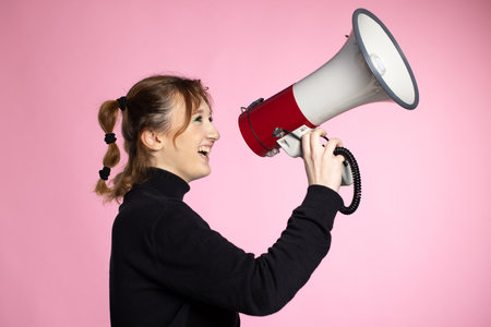 Funny young female shouting through megaphone. Young woman using loudspeaker on colored backgroundsの写真素材
