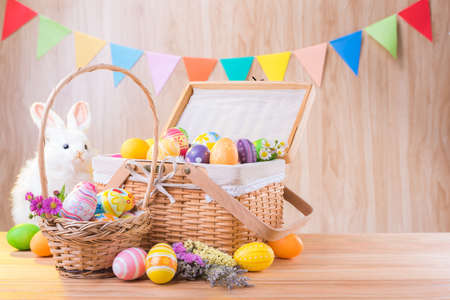 Happy Easter day colorful eggs and flowers in the basket with rabbit on wooden floor have blurred celebrate banner party flags.の写真素材