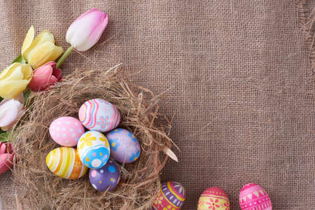 Happy Easter day eggs in nest and flower on wrinkled burlap fabric background with copy space.の写真素材