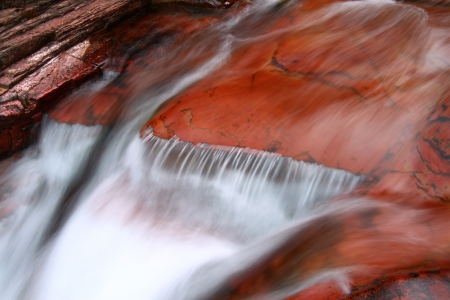 Smooth cascade over red rock in Glacier National Park of Montanaの写真素材