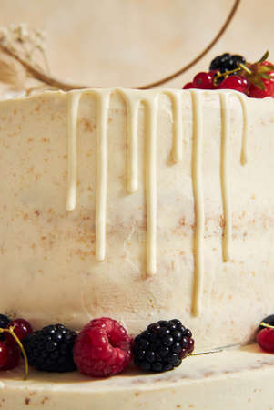 A vertical shot of a wedding cake decorated with fresh fruits and berries and a flower ring