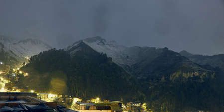 The houses surrounded by high mountains covered in snow in the evening