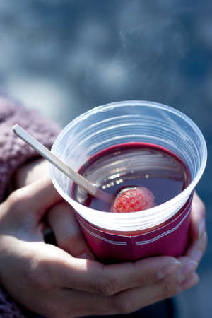 a close up shot of a person holding strawberry juice in a plastic cup in a blurry backgroundの写真素材