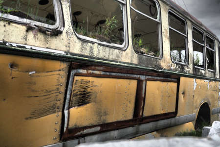 A closeup side view of an old abandoned wrecked bus in a field full of rubbishの写真素材