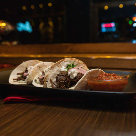 A closeup shot of delicious mexican pork carnitas tacos with salsa on a tray on the tableの写真素材
