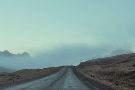A road surrounded by mountains covered in mist and cloudsの写真素材