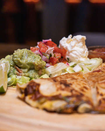 A closeup shot of delicious mexican quesadilla with grilled cheese, salad and lime on a wooden trayの写真素材