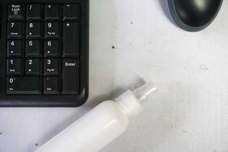 A high angle shot of a bottle of sanitizer by a keyboard and a mouse on a white desk