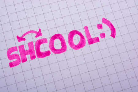 A closeup shot of a pink written text  "Shcool" with a reverse sign on paper with a smiley faceの写真素材