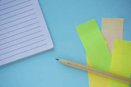 A high angel shot of a notebook pen pencil and colored note blank on blue table