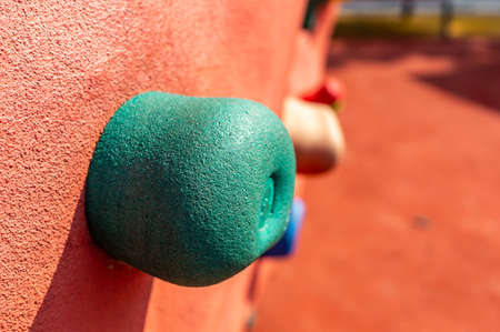 A small red rock formation with colorful handles for bouldering in the playground