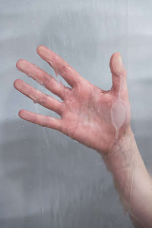 A vertical shot of a hand behind on a moist glass