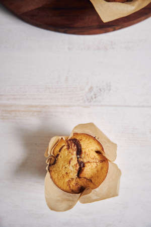 A vertical high angle shot of a delicious chocolate muffin near a wooden plate on a white plateの写真素材