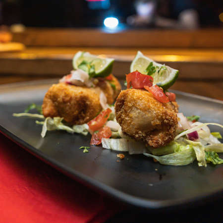 A closeup shot of fried mozzarella sticks with lime and salad in a black plate on the table