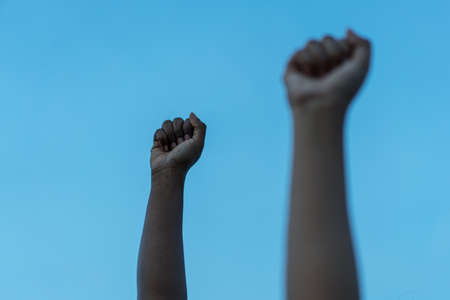 A closeup shot of African-American people raising hands on a blue background - the concept of combating racismの写真素材