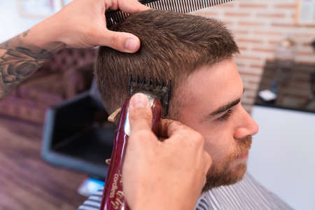 A young hairdresser cutting the male customer's hair with a hair clipper and a comb in a barbershopの写真素材