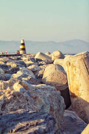 A vertical shot of the rocks of the beach with an old lighthouse visible in the backgroundの写真素材