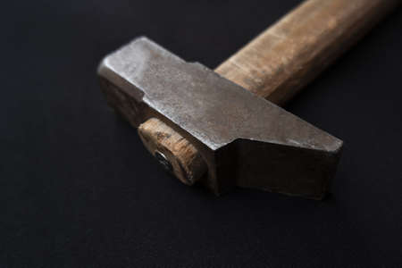 A closeup shot of a hammer with a wooden handle isolated on a black background