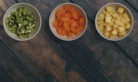 Three bowls with slices tangerine kiwi and pineapple on a wooden table