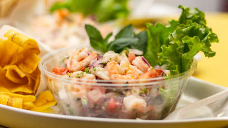 A closeup shot of delicious spicy shrimp salad in a bowl next to plantain chipsの写真素材