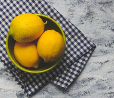 An overhead shot of three lemons in a bowl on the table with a towel on itの写真素材