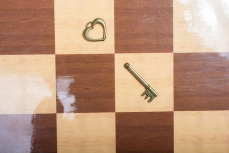 A close up shot of a romantic heart shaped vintage broken key on a chess pattern floorの写真素材