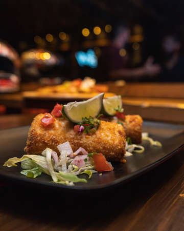 A closeup shot of fried mozzarella sticks with lime and salad in a black plate on the tableの写真素材